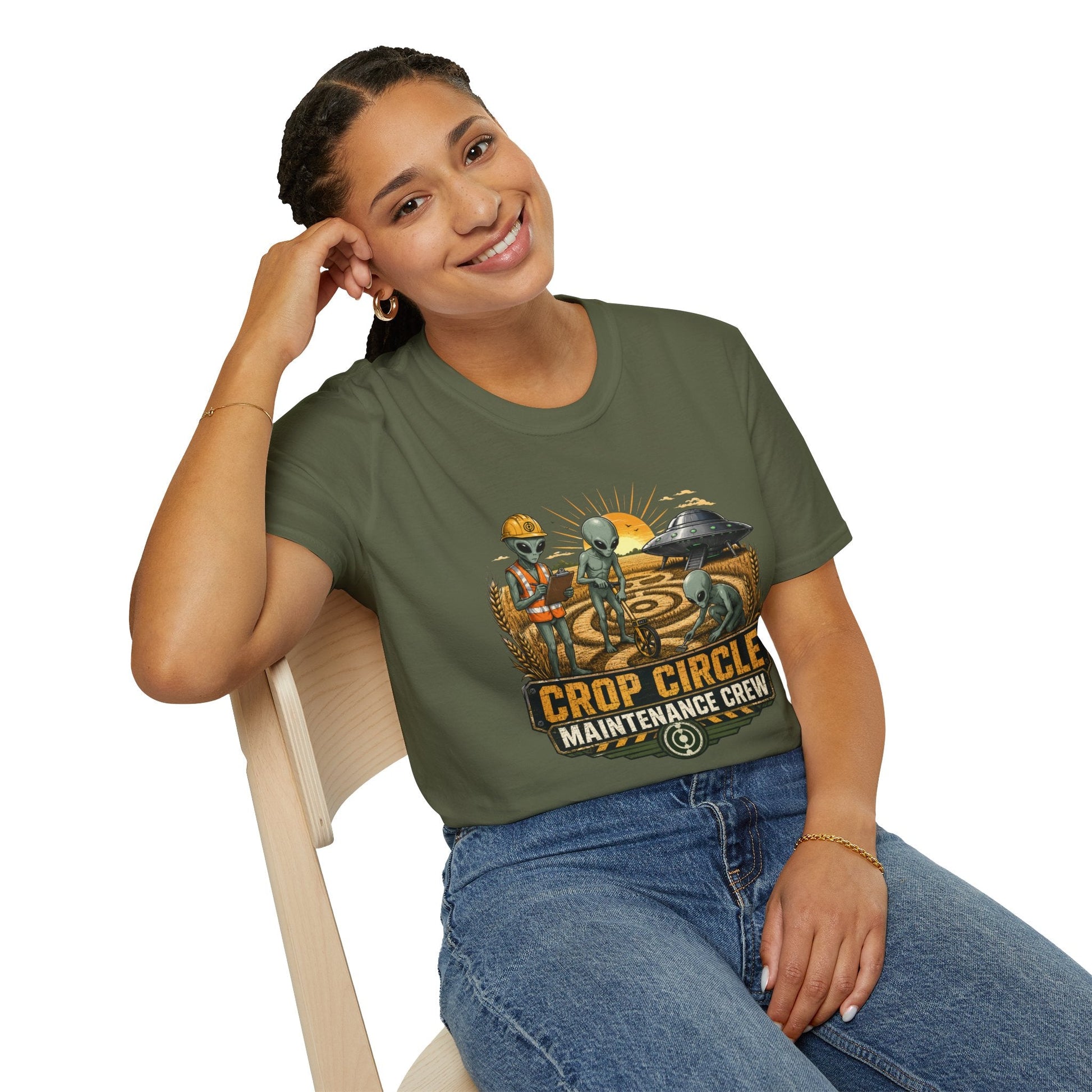 Model wearing the Crop Circle Maintenance Crew T-Shirt in military green featuring aliens working in a crop circle field with a UFO in the background.
