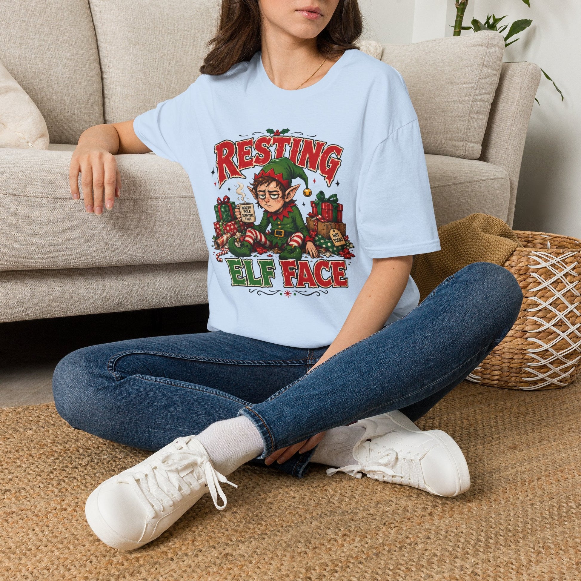 Model wearing the Resting Elf Face Christmas T-Shirt in light blue with funny tired elf artwork.