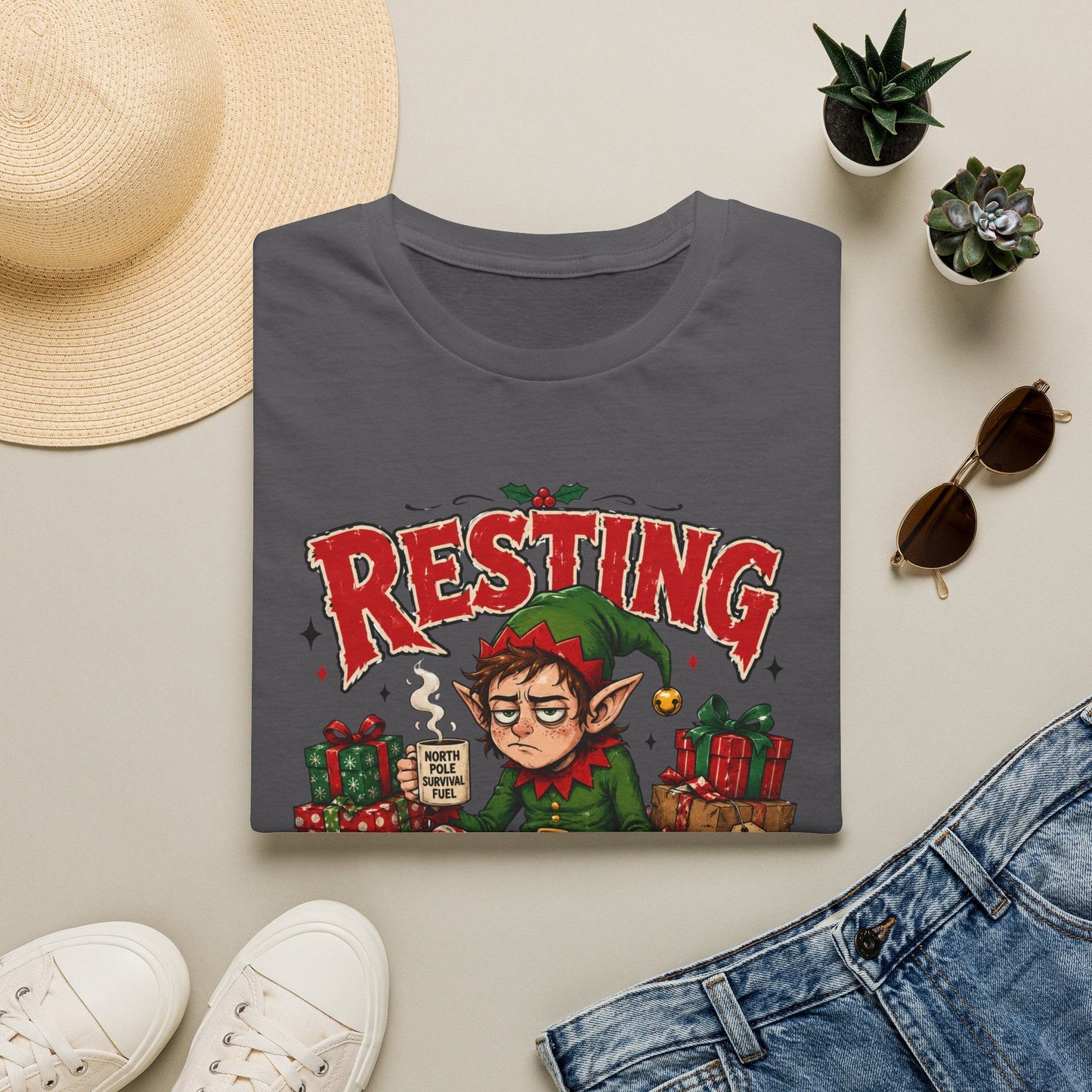 Folded Resting Elf Face Christmas T-Shirt in charcoal showing a funny Christmas elf graphic design.