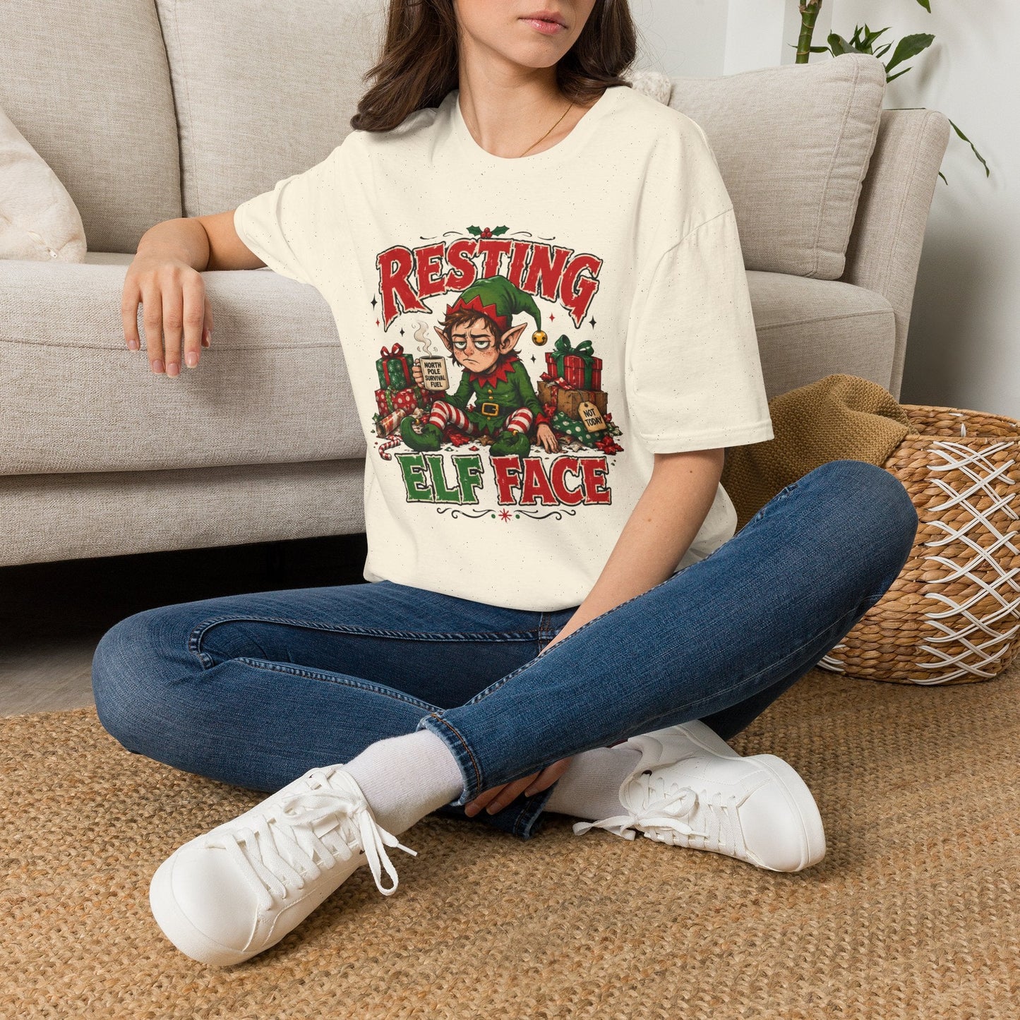 Model wearing the Resting Elf Face Christmas T-Shirt in natural with funny tired elf artwork.