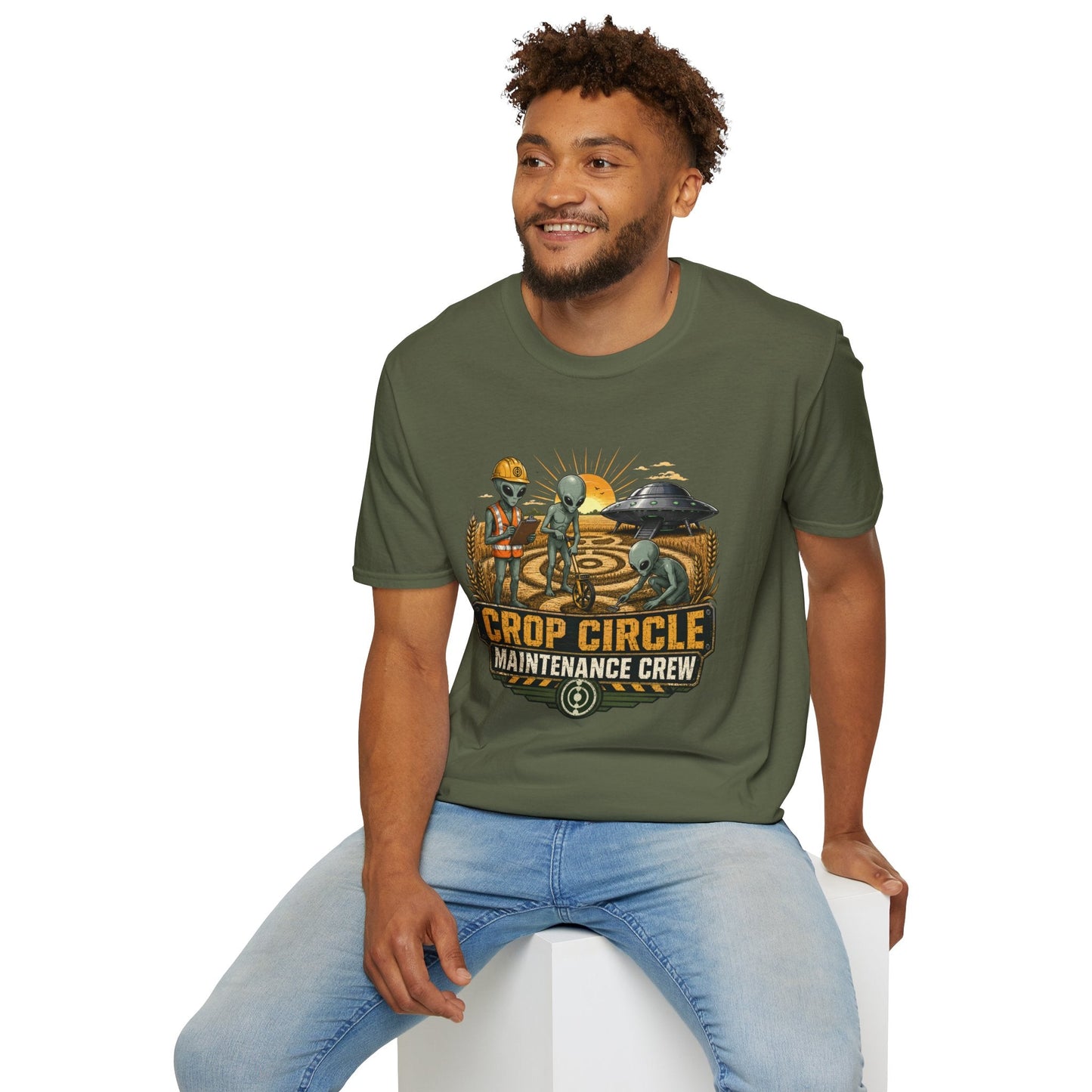 Model wearing the Crop Circle Maintenance Crew T-Shirt in military green featuring aliens working in a crop circle field with a UFO in the background.