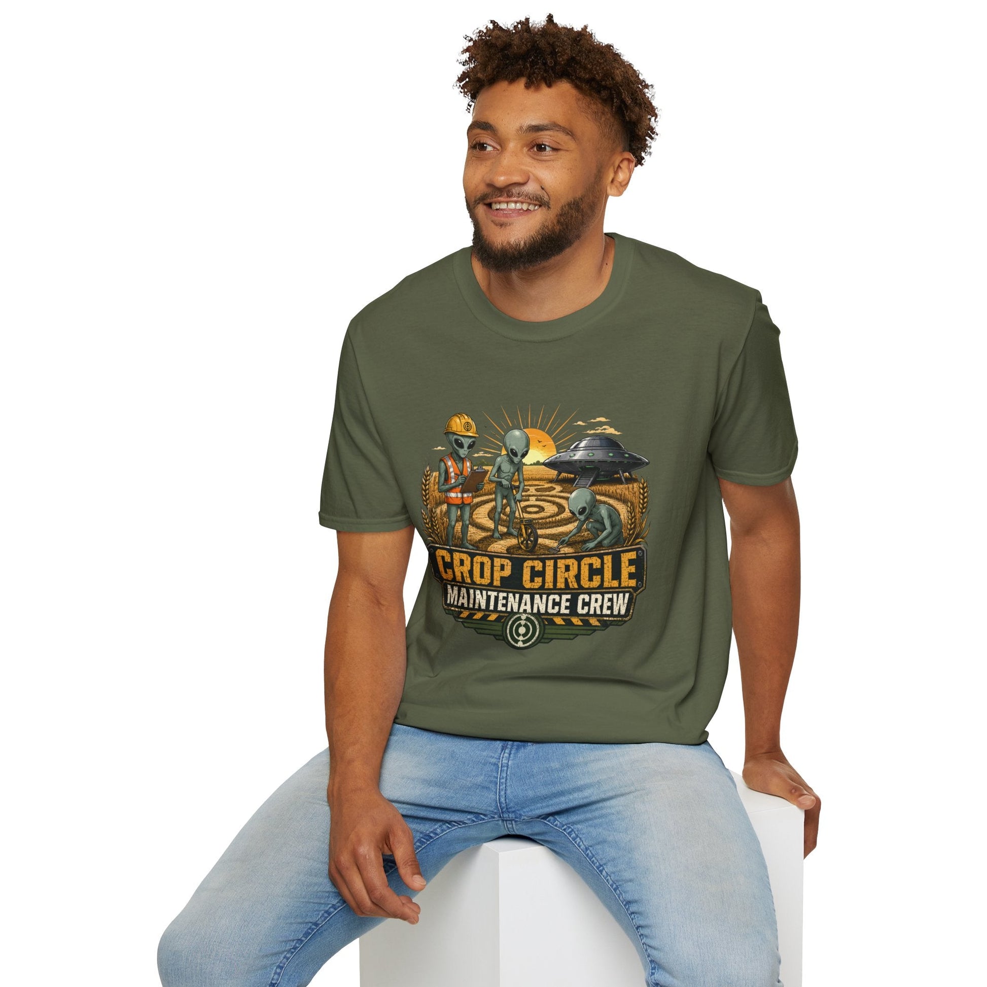 Model wearing the Crop Circle Maintenance Crew T-Shirt in military green featuring aliens working in a crop circle field with a UFO in the background.