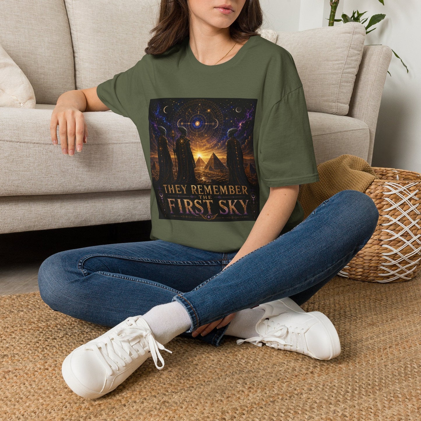 Model wearing the They Remember the First Sky T-Shirt in military green featuring robed alien watchers, pyramids, and a glowing celestial sky map design.