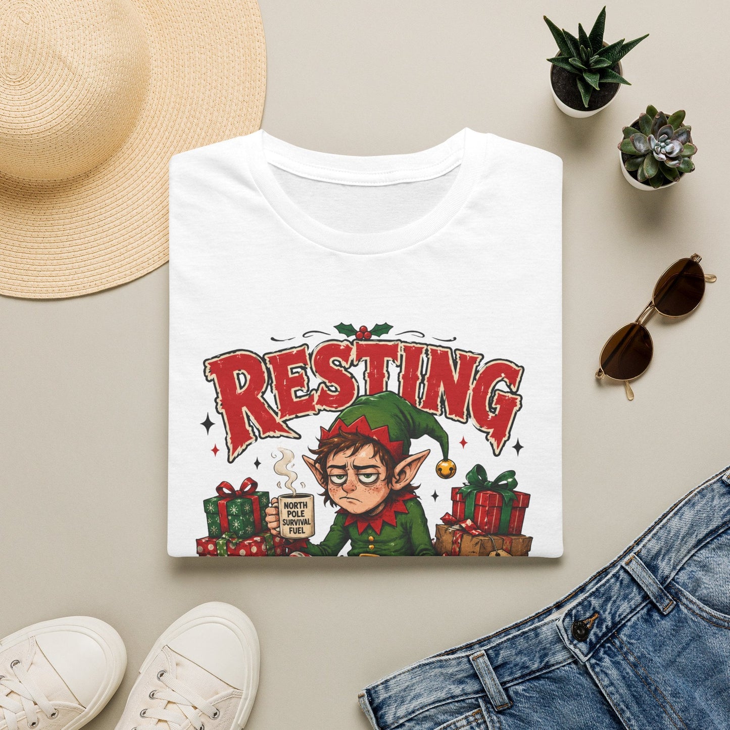 Folded Resting Elf Face Christmas T-Shirt in white showing a funny Christmas elf graphic design.